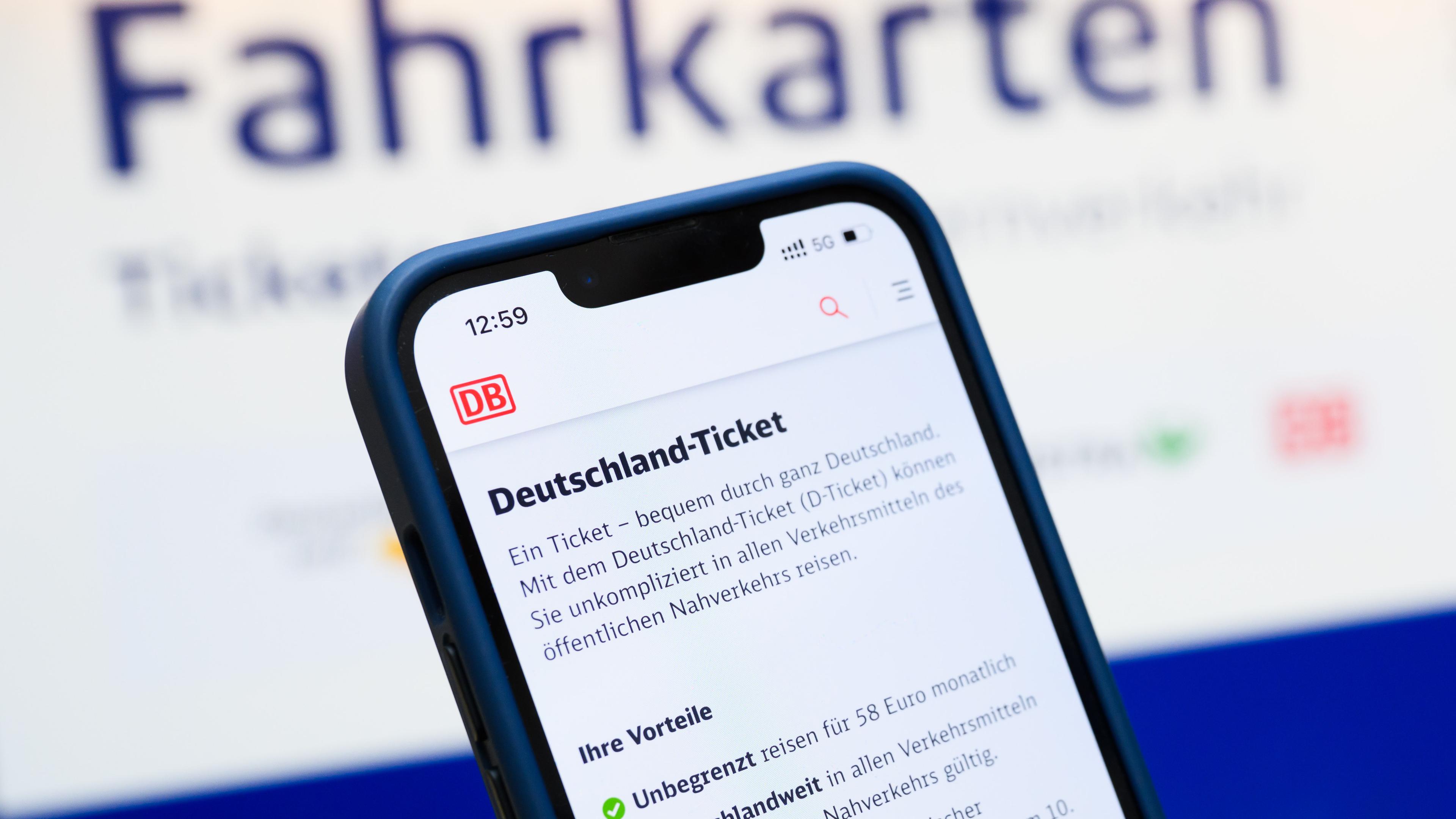 Eine Person hält am Hauptbahnhof ein Smartphone in der Hand, auf dessen Display eine Information zum Kauf des Deutschlandtickets zu sehen ist, während sie vor einem Fahrkartenautomaten steht. 