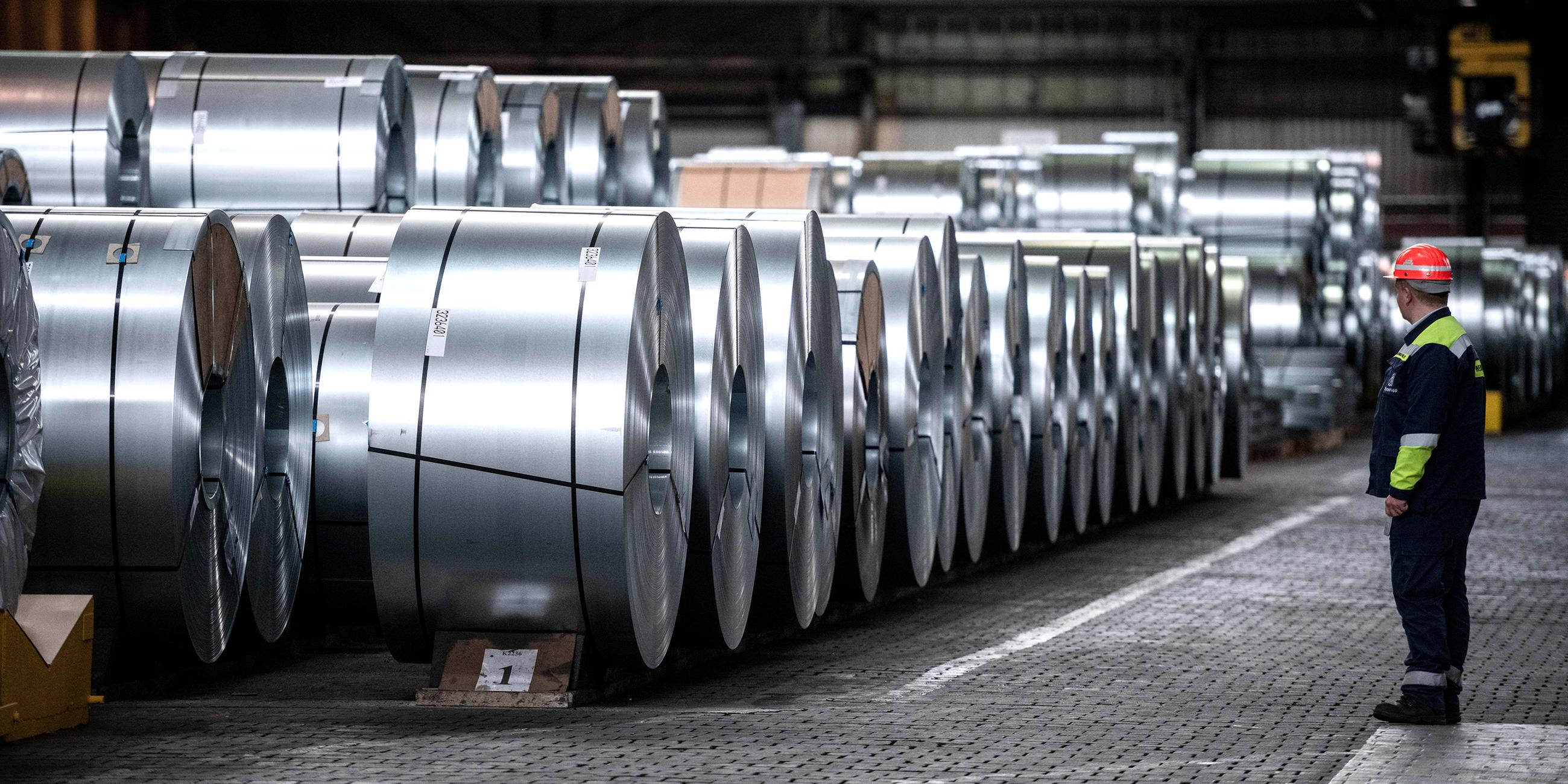 Ein Arbeiter steht vor Stahlspulen der Thyssenkrupp Steel Europe AG