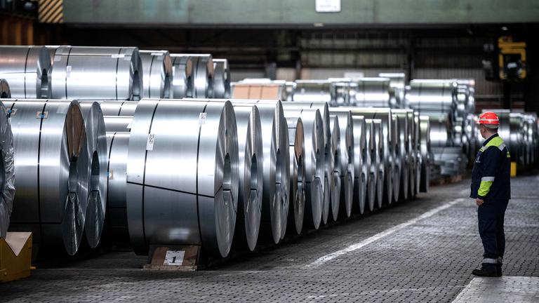 Ein Arbeiter steht vor Stahlspulen der Thyssenkrupp Steel Europe AG