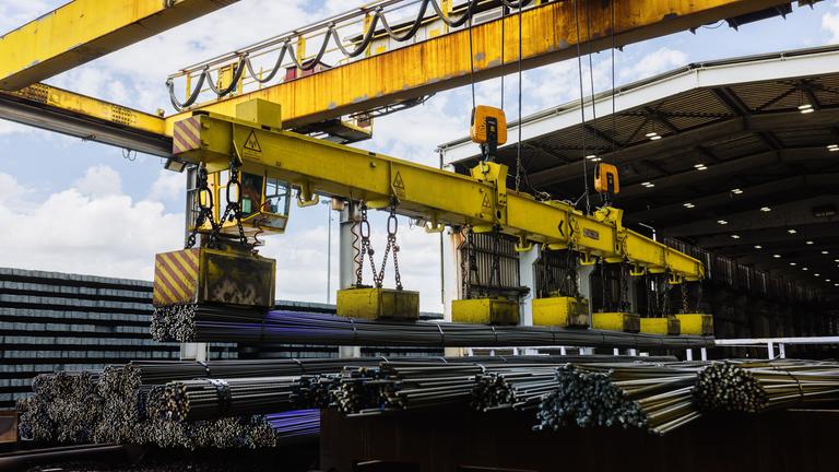 Ein Kran tranportiert frisch gewalzten Armierungsstahl. 