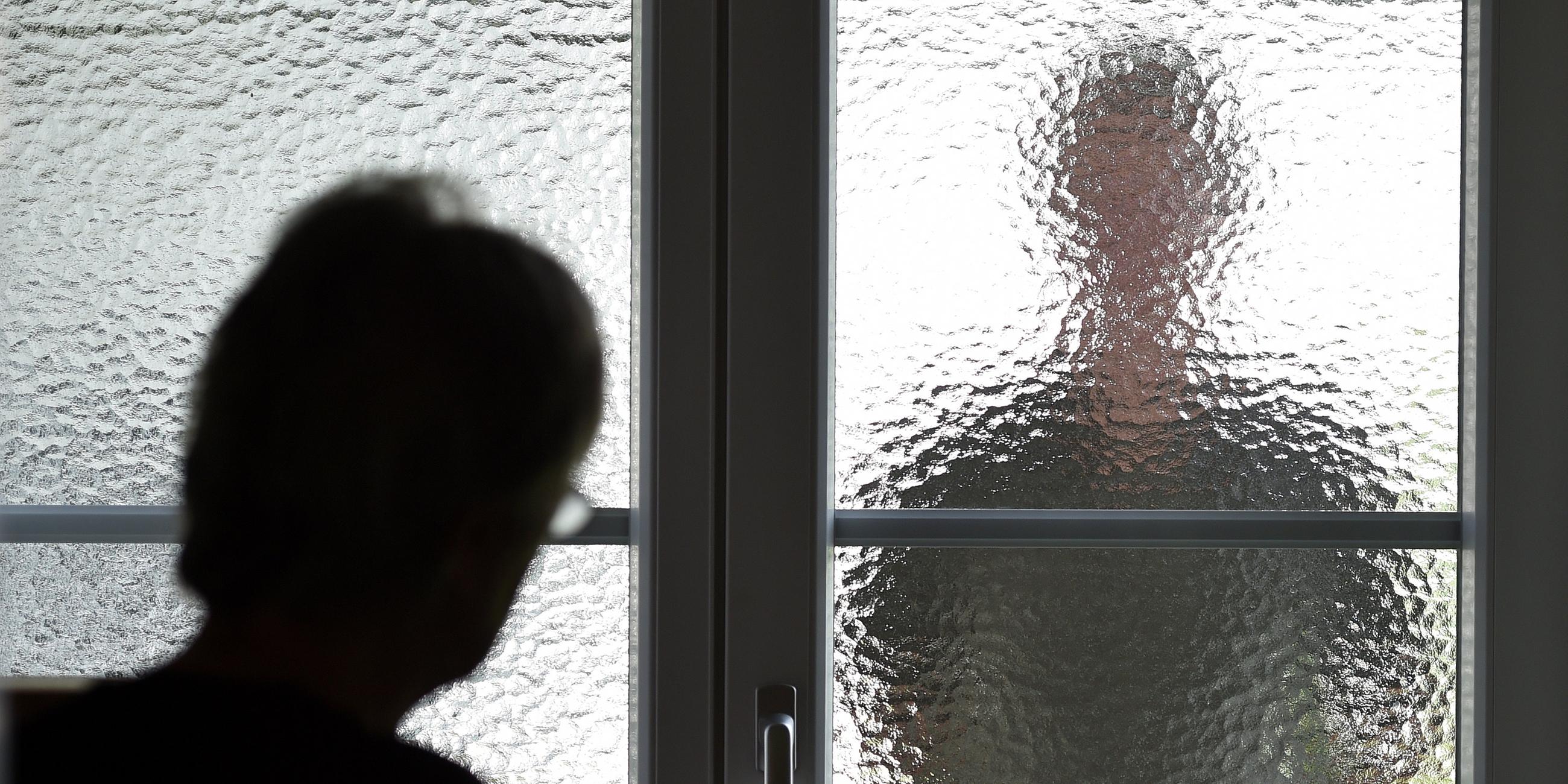 Eine Frau steht an einer Glasscheibe, hinter der ein Stalker steht.