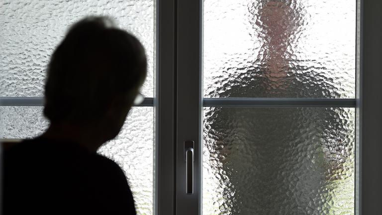 Eine Frau steht an einer Glasscheibe, hinter der ein Stalker steht.