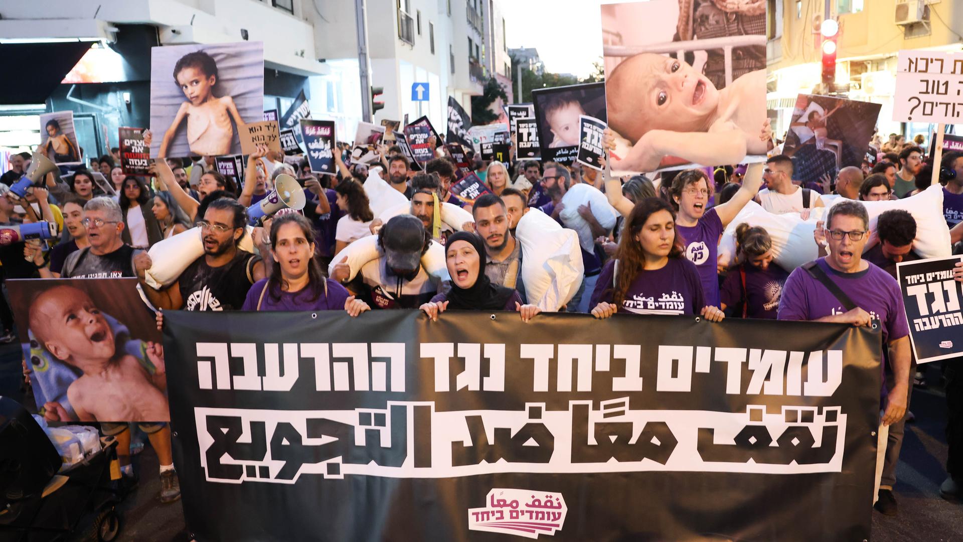 Israelische und arabische Aktivisten tragen am 22.07.2025 in Tel Aviv Mehltüten und ein Banner mit der Aufschrift „Gemeinsam gegen Hunger“ bei einer Kundgebung gegen den Krieg und die Hungersnot in Gaza.