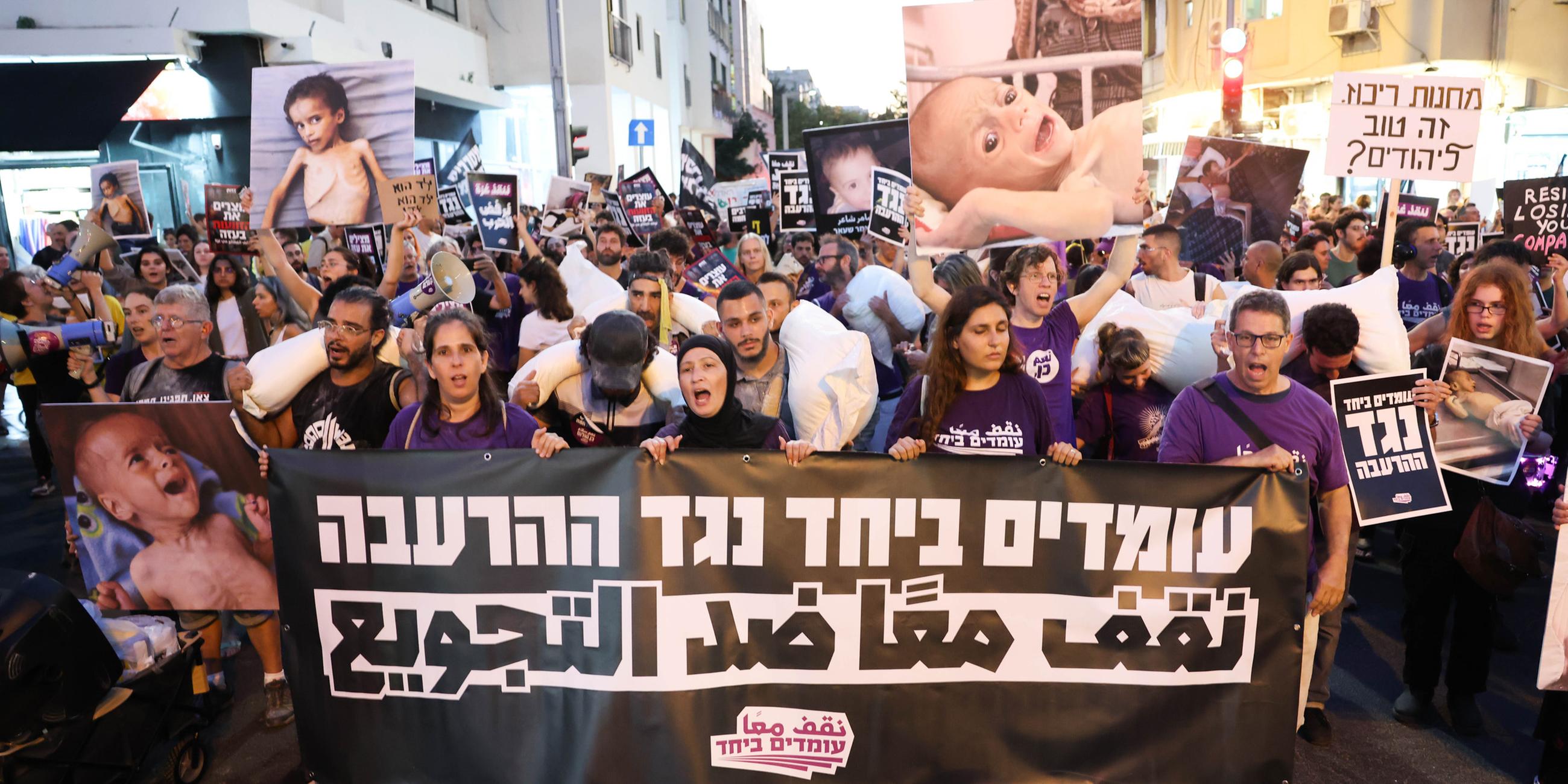 Israelische und arabische Aktivisten tragen am 22.07.2025 in Tel Aviv Mehltüten und ein Banner mit der Aufschrift „Gemeinsam gegen Hunger“ bei einer Kundgebung gegen den Krieg und die Hungersnot in Gaza.