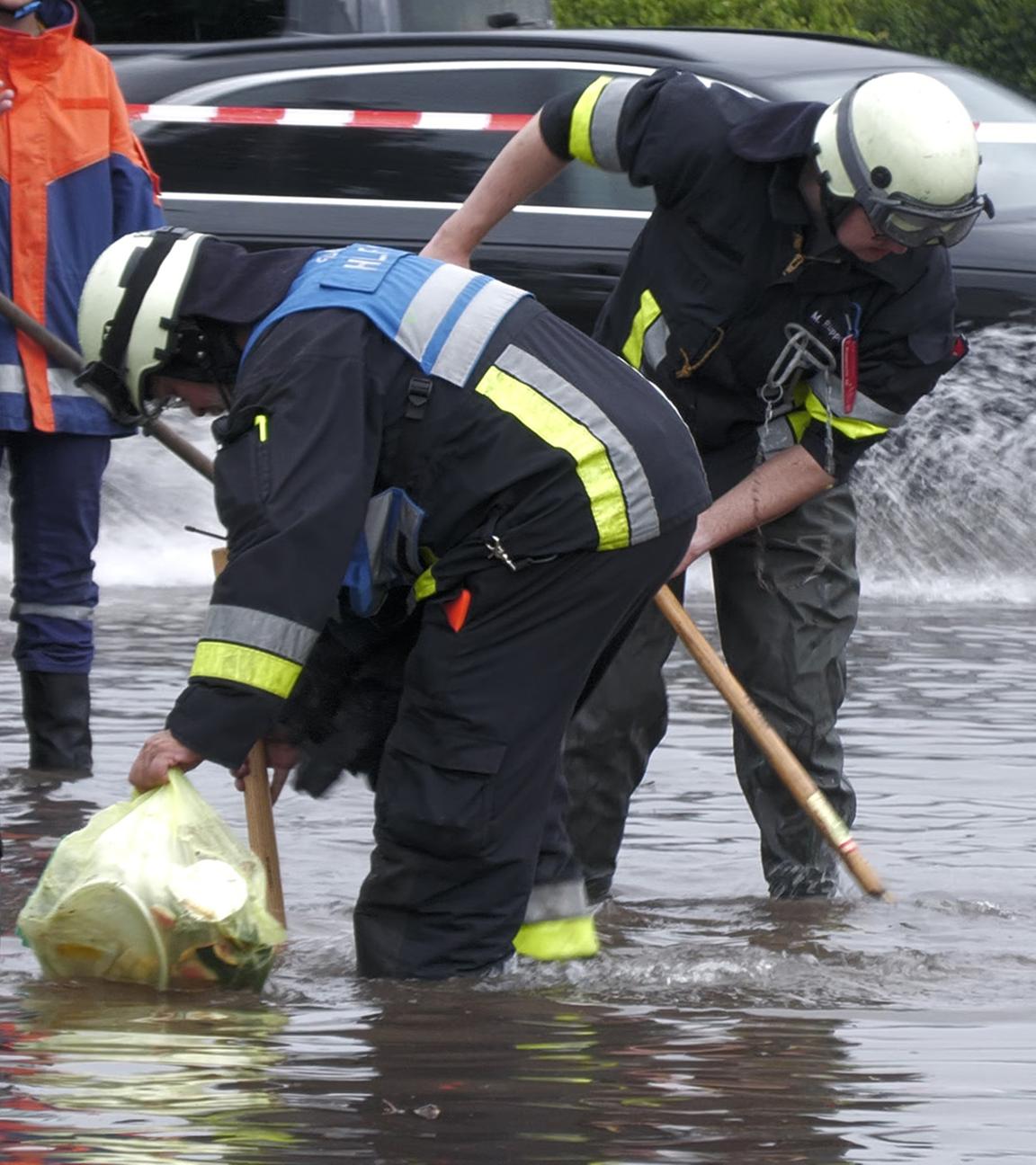  Feuerwehrleute öffnet Gullys auf einer unter Wasser stehenden Straße. Heftige Regenfälle haben am 26.07.2025 in Teilen Bayerns Straßen überflutet und Keller unter Wasser gesetzt.