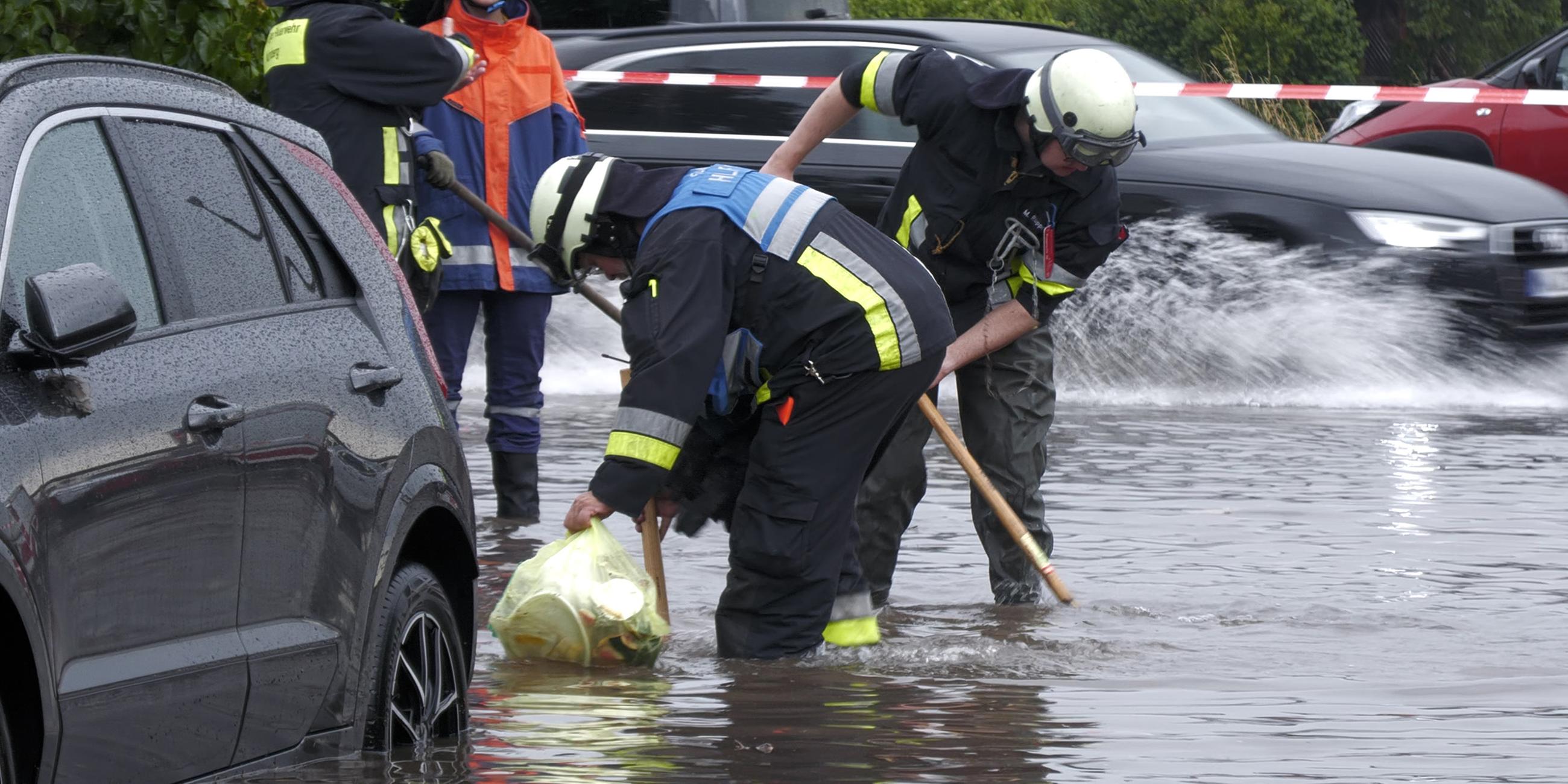  Feuerwehrleute öffnet Gullys auf einer unter Wasser stehenden Straße. Heftige Regenfälle haben am 26.07.2025 in Teilen Bayerns Straßen überflutet und Keller unter Wasser gesetzt.
