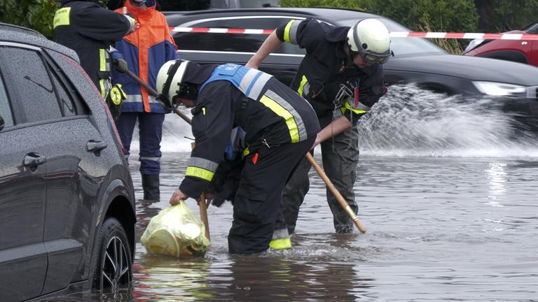  Feuerwehrleute öffnet Gullys auf einer unter Wasser stehenden Straße. Heftige Regenfälle haben am 26.07.2025 in Teilen Bayerns Straßen überflutet und Keller unter Wasser gesetzt.
