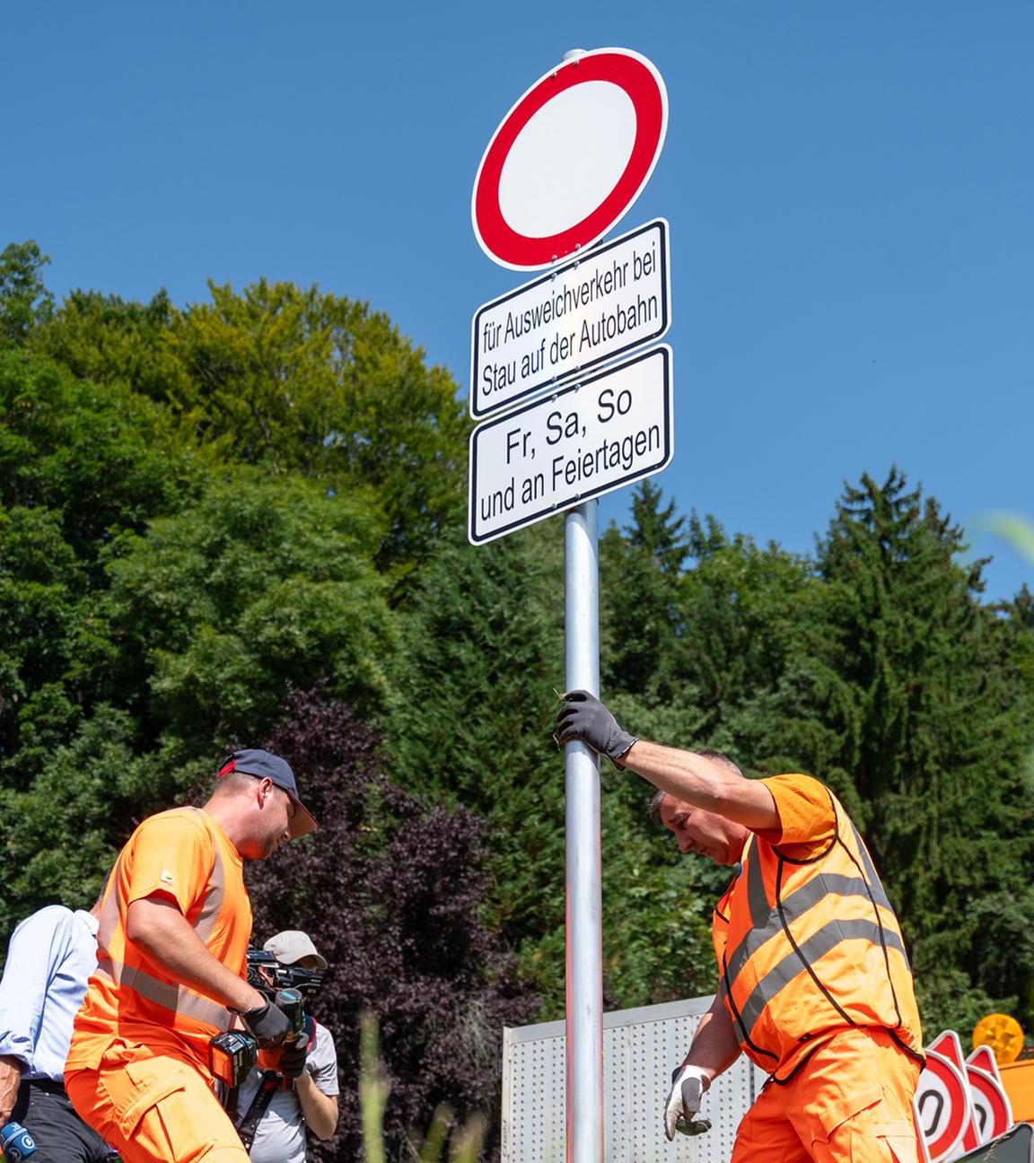 Mitarbeiter der Straßenmeisterei des Staatlichen Bauamtes Rosenheim und dem Bauhof des Landkreises Rosenheim stellen Schilder an einer Straße auf.