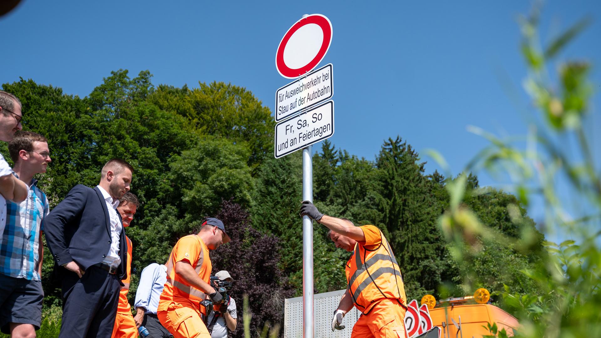 Mitarbeiter der Straßenmeisterei des Staatlichen Bauamtes Rosenheim und dem Bauhof des Landkreises Rosenheim stellen Schilder an einer Straße auf.