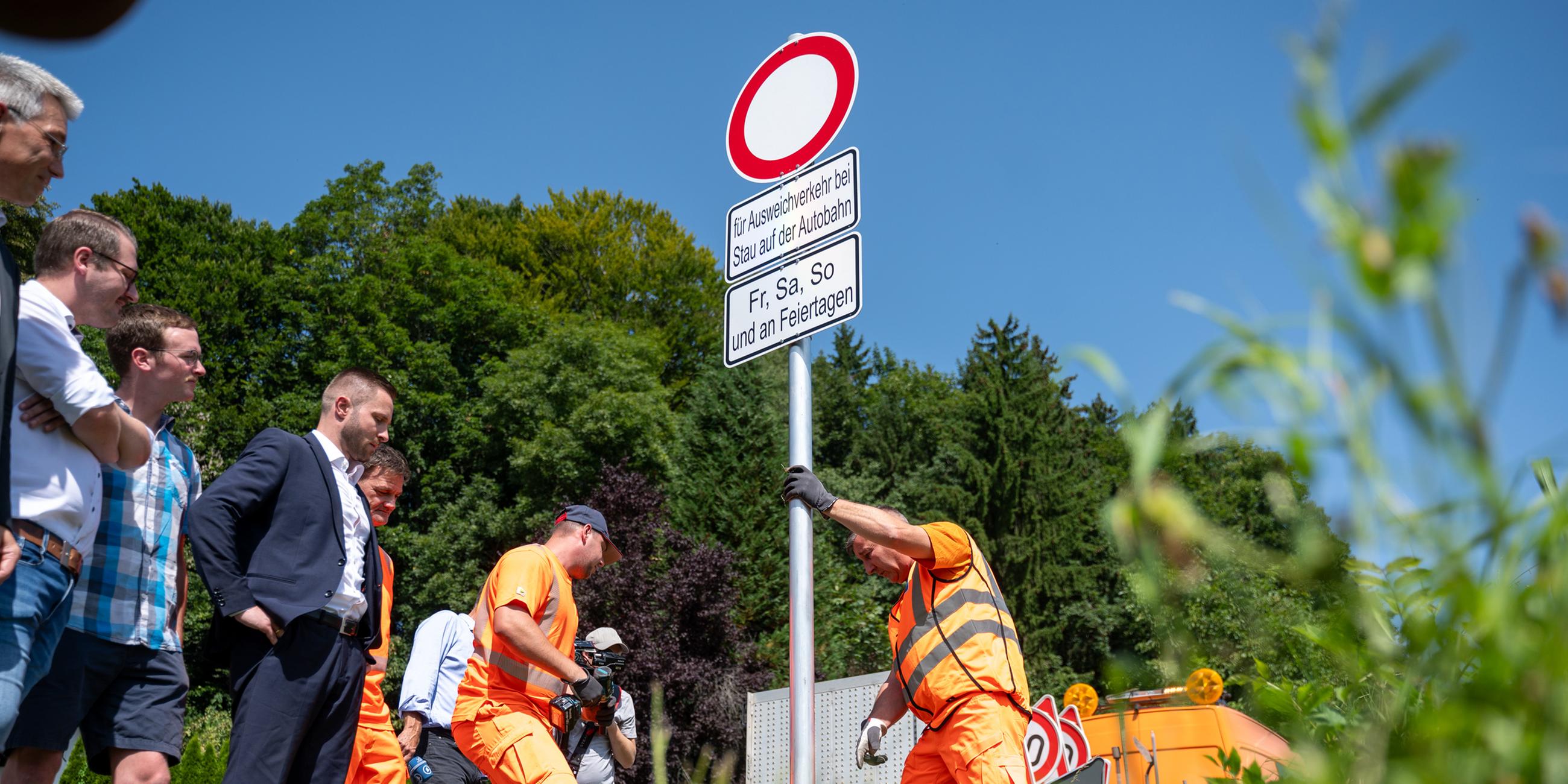 Mitarbeiter der Straßenmeisterei des Staatlichen Bauamtes Rosenheim und dem Bauhof des Landkreises Rosenheim stellen Schilder an einer Straße auf.