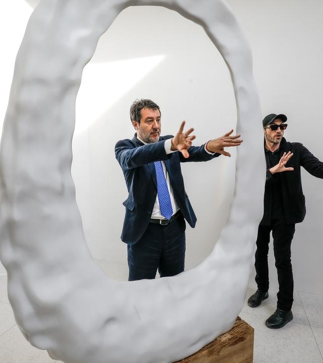 Italiens stellvertretender Ministerpräsident Matteo Salvini (l) besucht den Pavillon der Vereinigten Staaten. Es ist ein weißer Raum mit einer weißen ovalförmigen Skulptur.