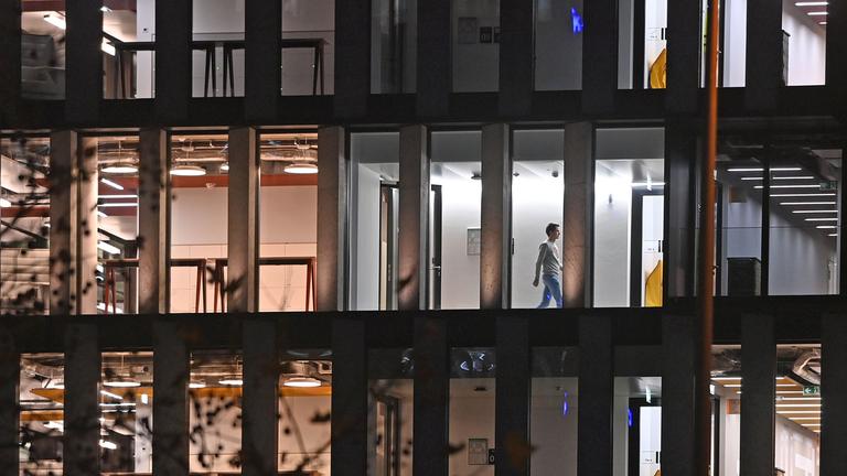 Beleuchtete und unbeleuchtete Büros in einem Bürogebäude sind von außen zu sehen. Eine Person läuft über den Flur.