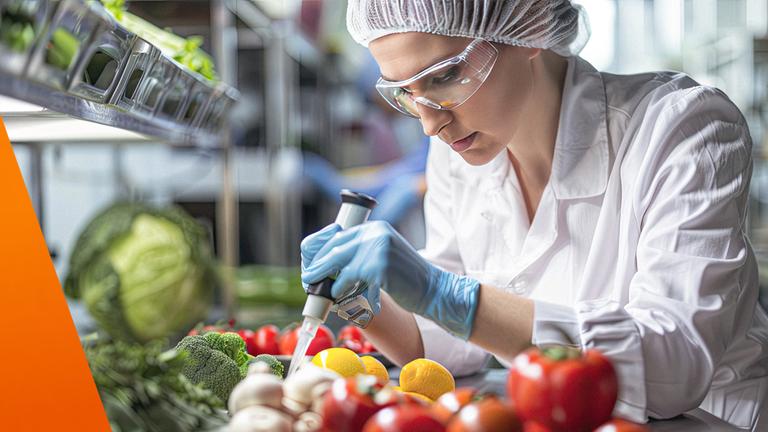 Frau mit weißem Kittel und Schutzbrille arbeitet mit einer Spritze an verschiedene Gemüsesorten