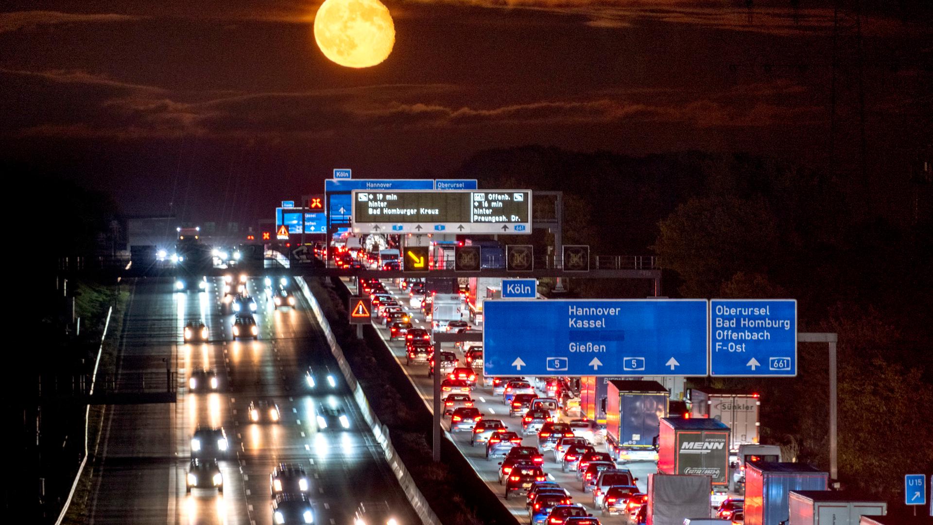 Symbolbild: Autos und Lastwagen stehen auf einer Autobahn bei Frankfurt im Stau, während der Mond aufgeht. 