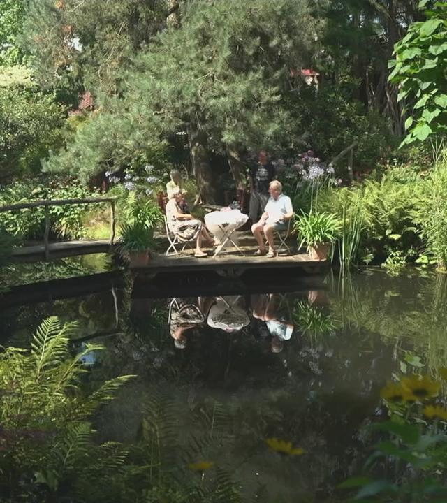 Zwei Menschen sitzen im Garten vor einem See