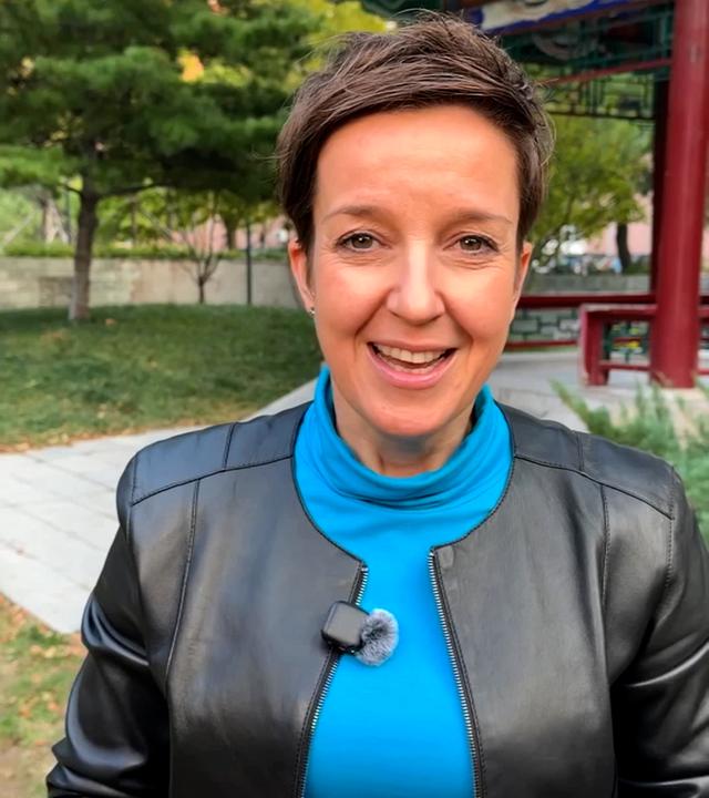 Miriam Steimer steht in schwarzer Lederjacke und blauem Oberteil vor einem chinesischen Tempel. Sie hat ihre beiden Hände vor dem Bauch ineinander verschlungen.