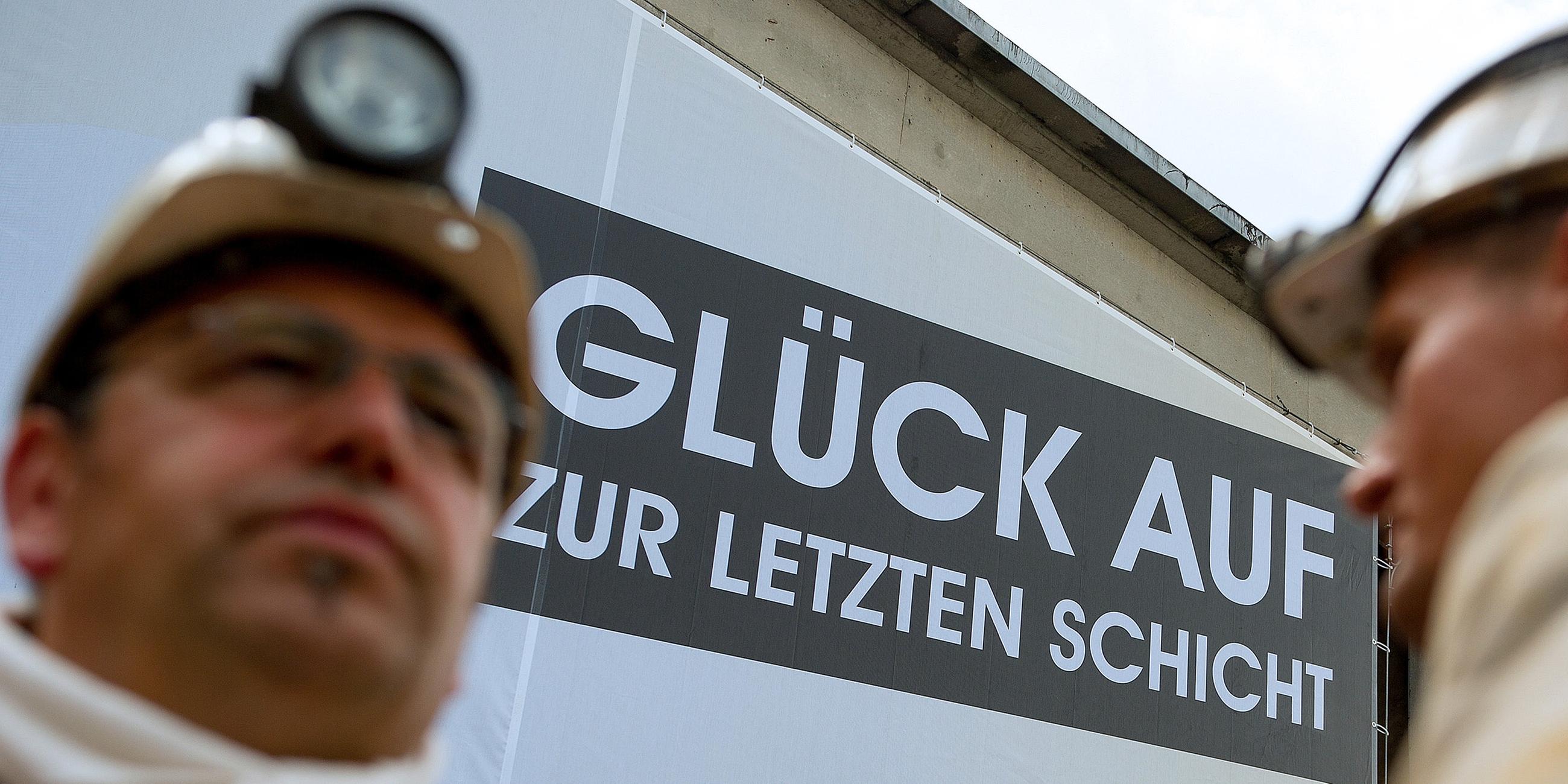 Archiv: Zwei Bergmänner vor einem Plakat mit der Aufschrift "Glück auf zur letzten Schicht"