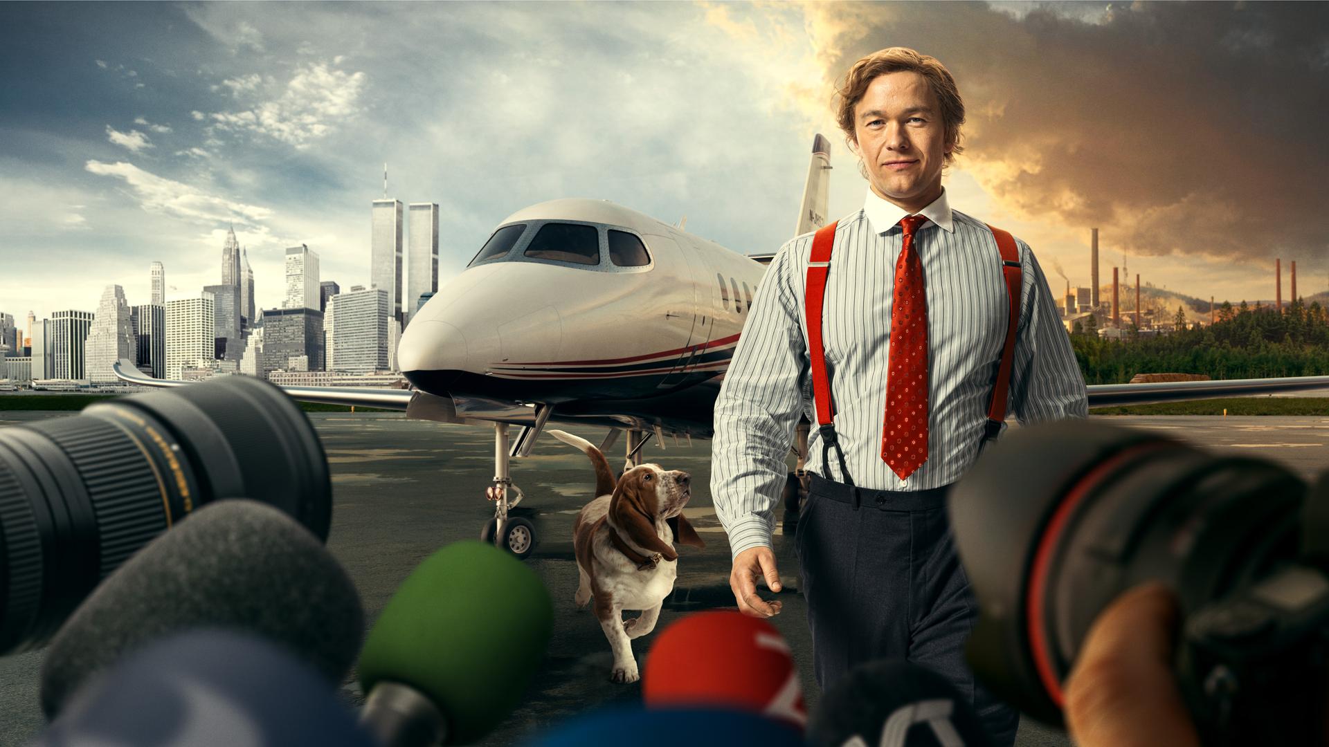 Stenbeck steht, in einem gestreiften Hemd mit roter Krawatte und roten Hosenträgern, auf einem Flugfeld. Sein Hund, ein braun-weißer Basset, schaut von links unten hoch zu ihm. Direkt hinter ihm steht ein moderner Privat-Jet. Im Hintergrund sieht man eine geteilte Landschaft, links die New Yorker Skyline, rechts eine ländliche Landschaft mit einer rauchenden Fabrik darauf. Der Himmel über New York ist weitgehend klar und blau, über der Fabrik ziehen dunkle, rötlich gefärbte Wolken. Im Vordergrund sind Kameras und Mikrofone aufgebaut.