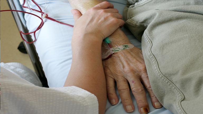 Archiv: Ein Pfleger hölt die Hand einer sterbenden Person