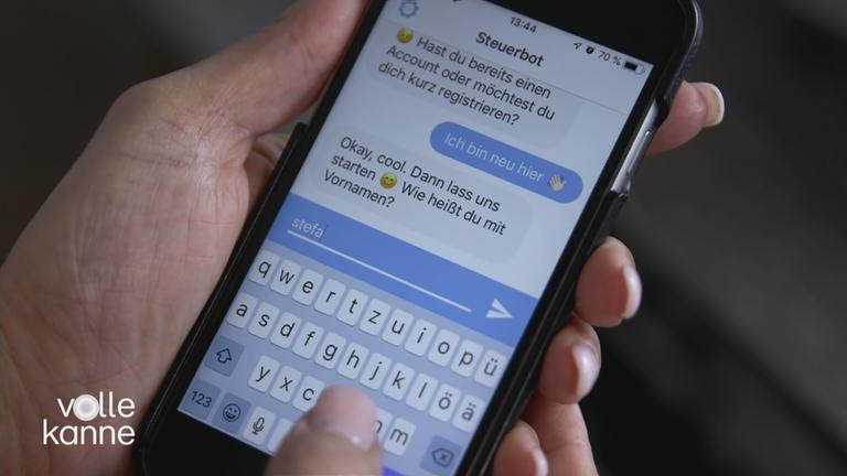 Ein Handy in einer Hand. Auf dem Handy ist ein Chat mit dem "Steuerbot" offen.