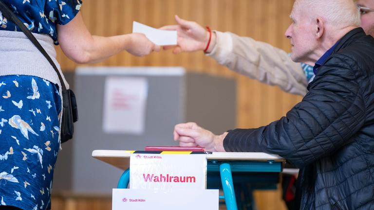 Ein Wahlhelfer übergibt ein einen Stimmzettel zur Stichwahl im Wahlraum 