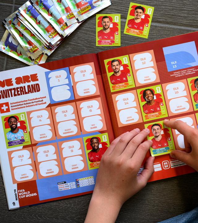 Ein junger Sammler klebt einen Panini-WM-Sticker der Schweizer Fußballnationalmannschaft in das offizielle Panini-Album zur FIFA-Weltmeisterschaft 2026