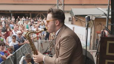 Ein Mann spielt Saxophon auf einer Bühne vor einer Menschenmenge