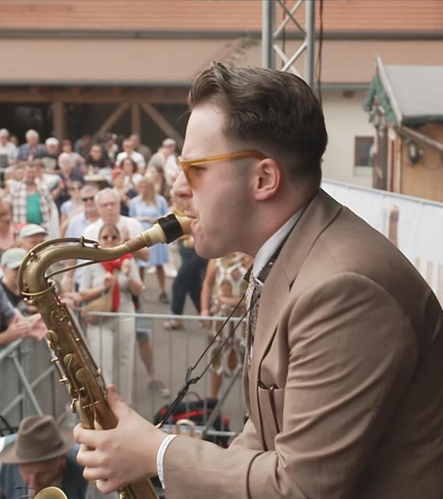 Ein Mann spielt Saxophon auf einer Bühne vor einer Menschenmenge