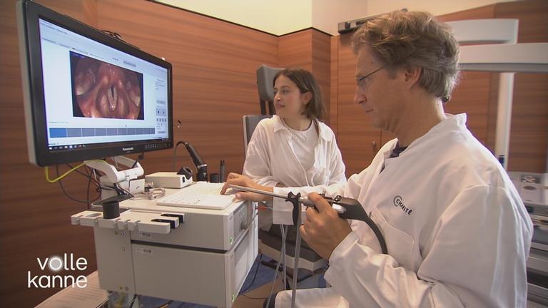 Eine Patientin sitzt beim Arzt und schaut sich gemeinsam mit ihm ein Bild ihrer Stimmlippenknötchen auf dem PC an.