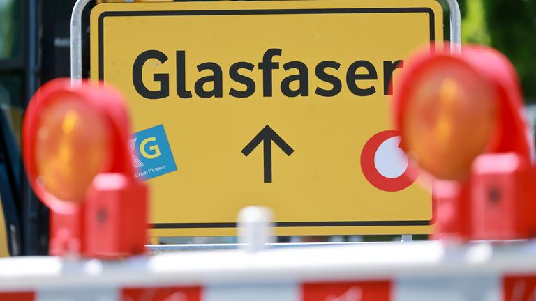 Ein gelbes Schild mit der Schrift "Glasfaserausbau". Um das Schild herum stehen Baustellenabkrezungen.