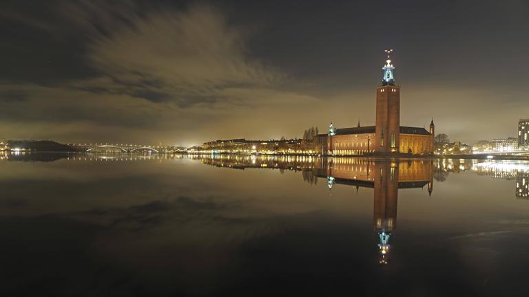 Nächtliche Stadtansicht vom schwedischen Stockholm mit beleuchtetem Turm und Brücken im Hintergrund.