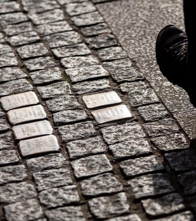 Ein Fuß ist rechts neben sechs Stolpersteinen zu sehen.