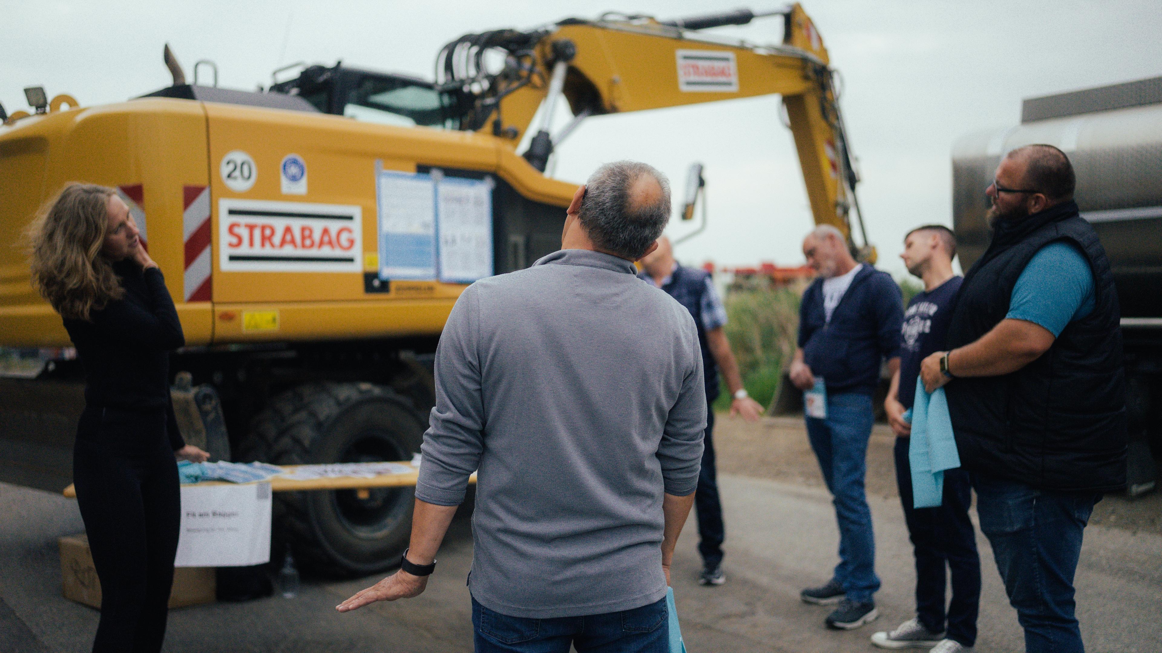 Mehrere Bauarbeiter stehen auf einer Baustelle im Kreis und machen körperliche Übungen