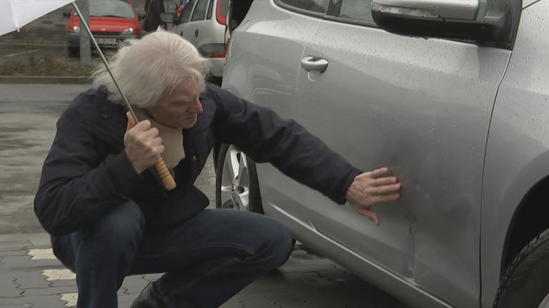 Auf dem Bild ist ein Mann zu sehen, der gerade sein kaputtes Auto anschaut.