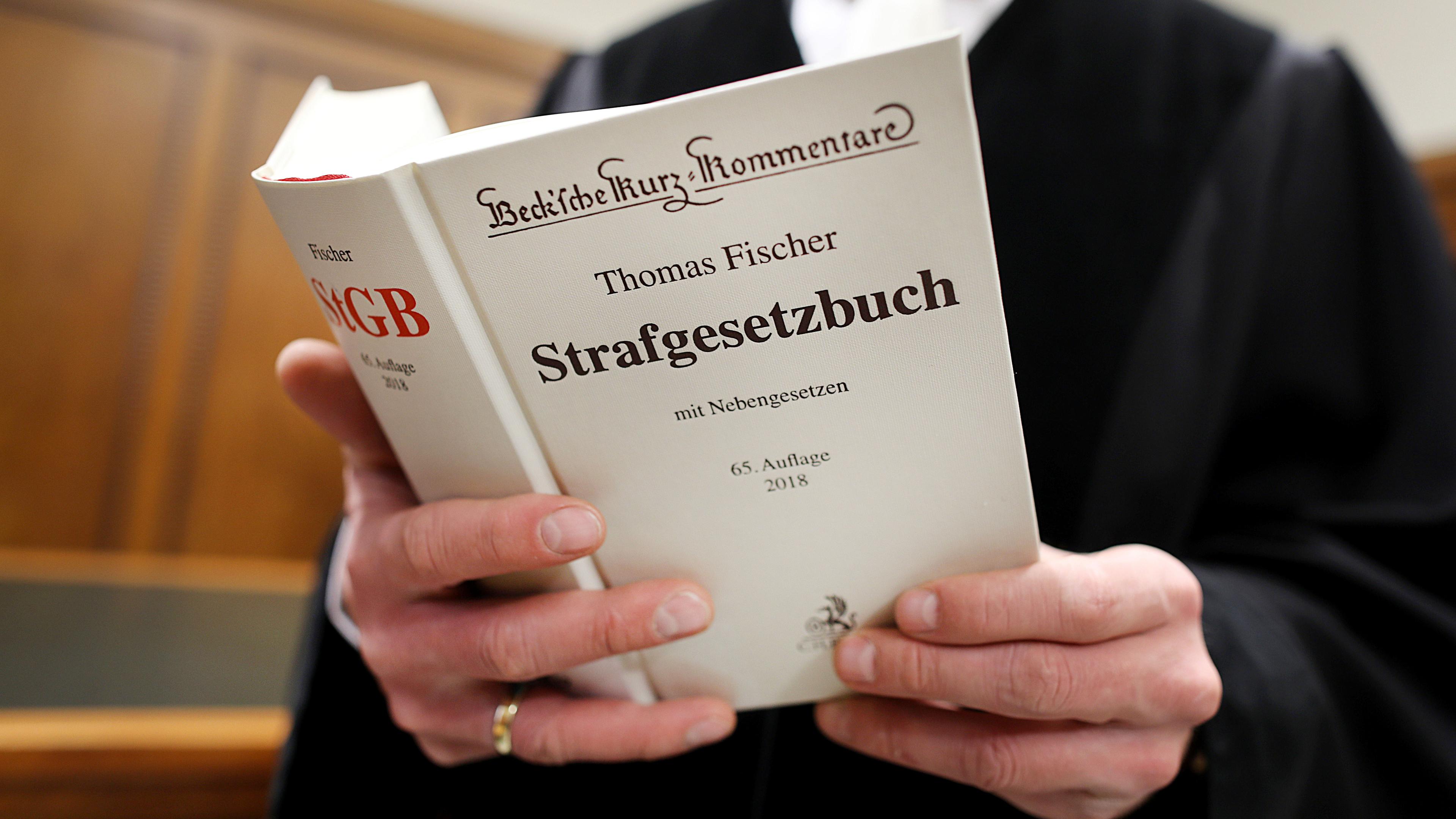 Ein Richter im Gerichtssaal hält das Strafgesetzbuch (StGB) in der Hand.