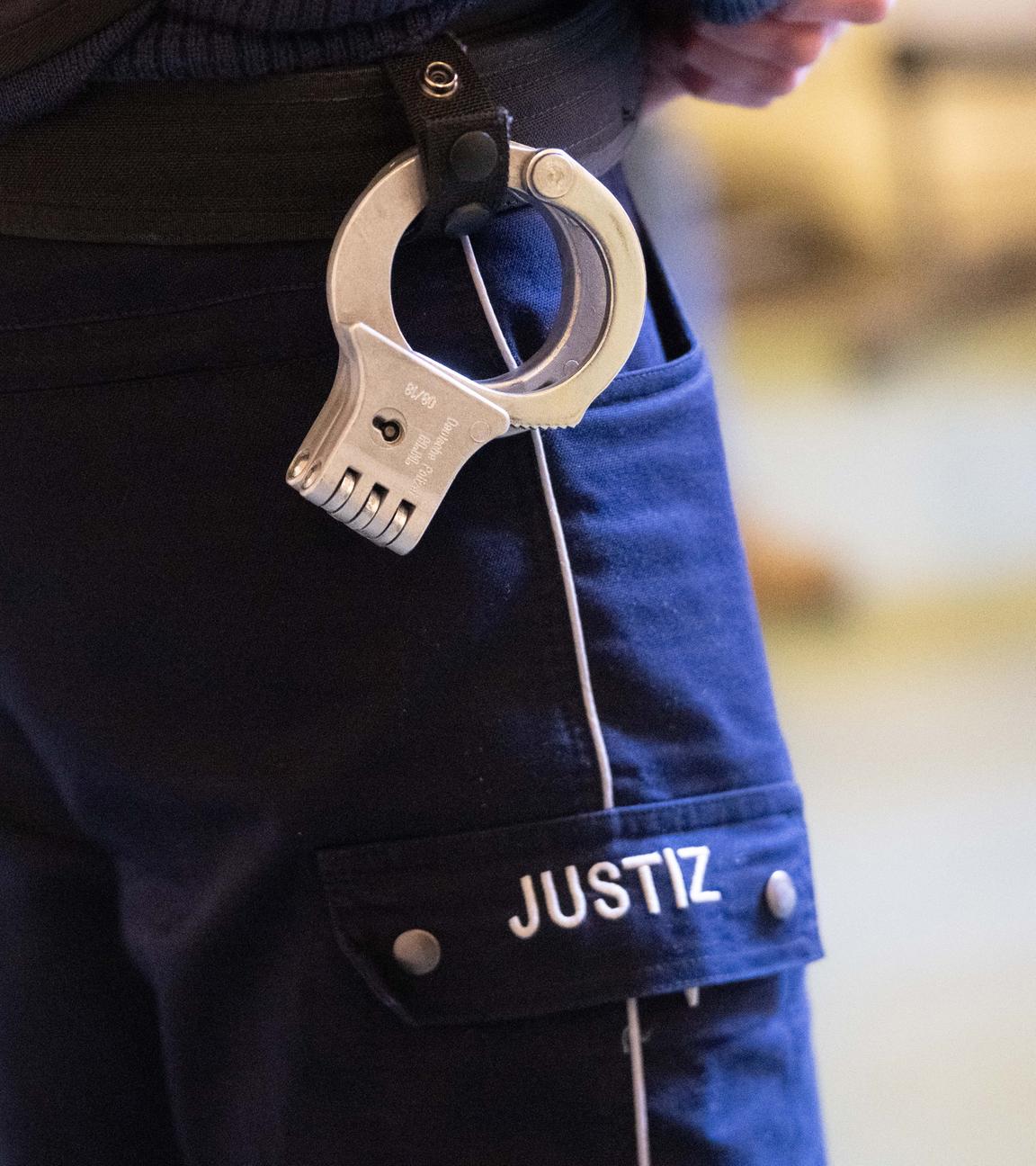 Symbolbild: Ein Justizbeamter mit Handschellen am Gürtel steht im Verhandlungssaal eines Verwaltungsgerichts in Nordrhein-Westfalen