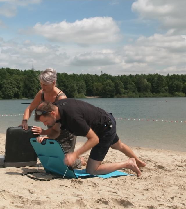 Eine Mann und eine Frau bauen am Strand eine Liege auf