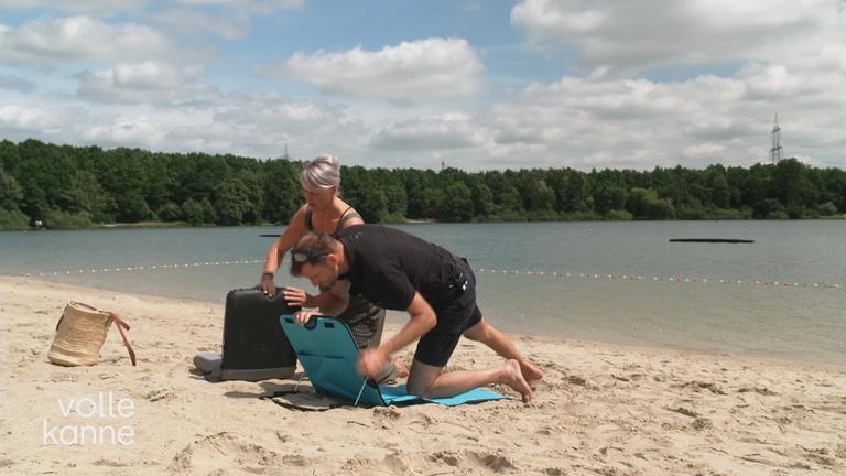 Eine Mann und eine Frau bauen am Strand eine Liege auf