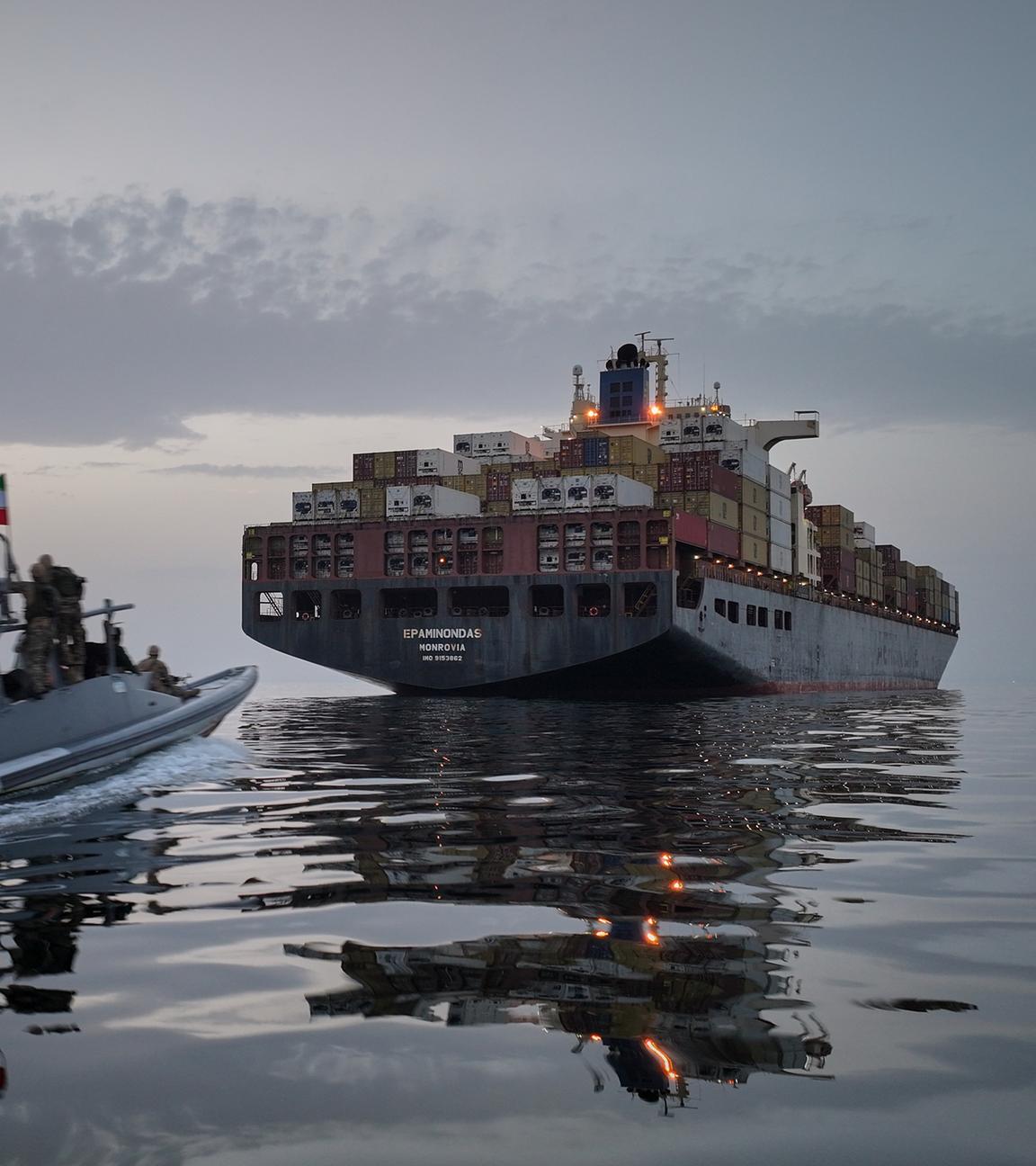 Iranisches Motorboot fährt in der Straße von Hormus einem Containerschiff hinterher.