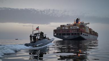 Iranisches Motorboot fährt in der Straße von Hormus einem Containerschiff hinterher.