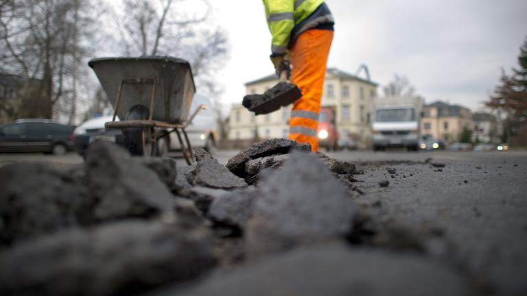 Ein Mitarbeiter einer Straßenbaufirma beseitigt in Dresden Straßenschäden