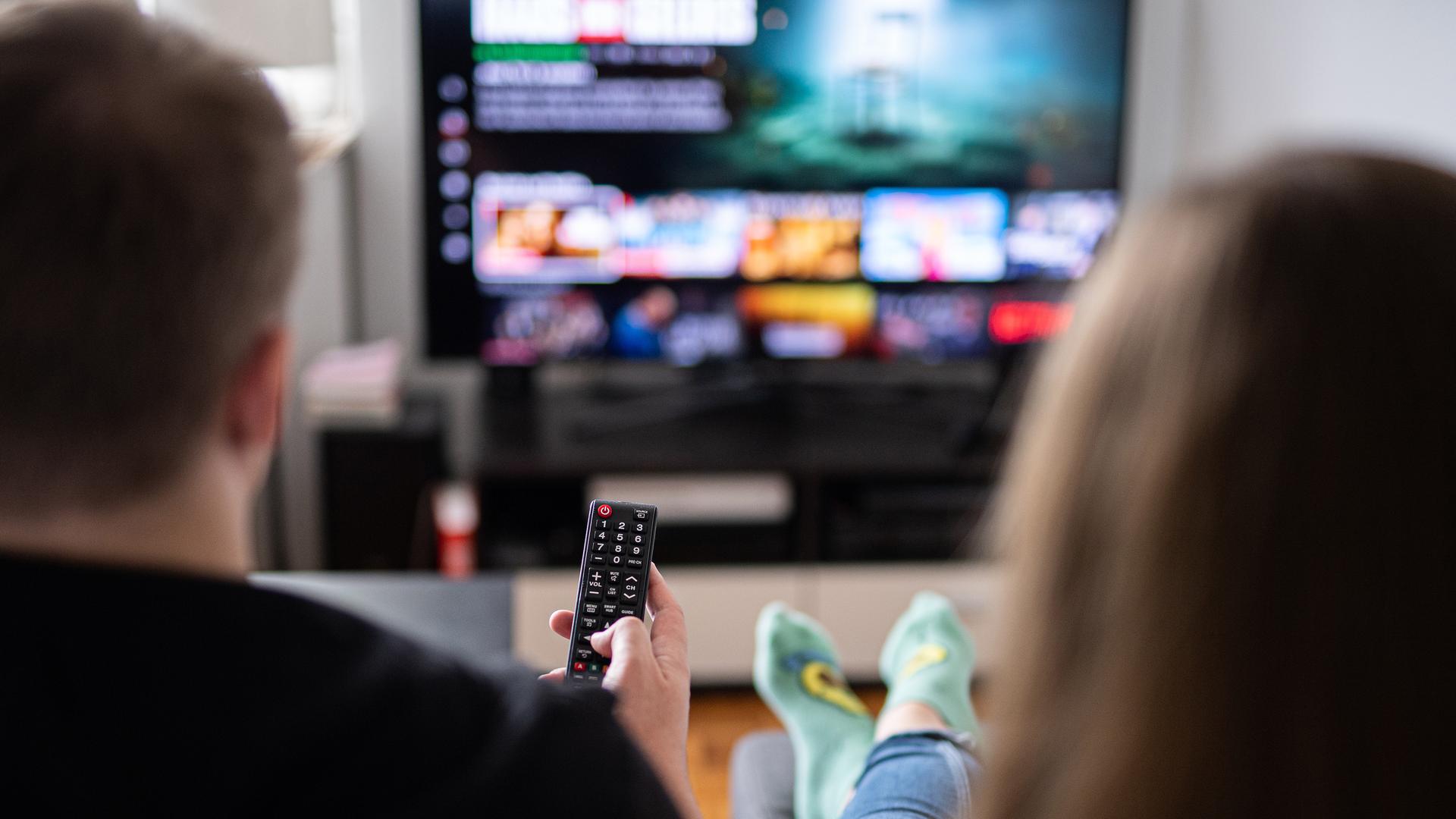 Ein Paar sitzt vor dem Fernseher, der Mann hält die Fernbedienung