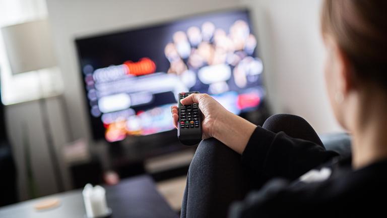 Eine Person sitzt vor dem Fernseher und hält eine Fernbedienung