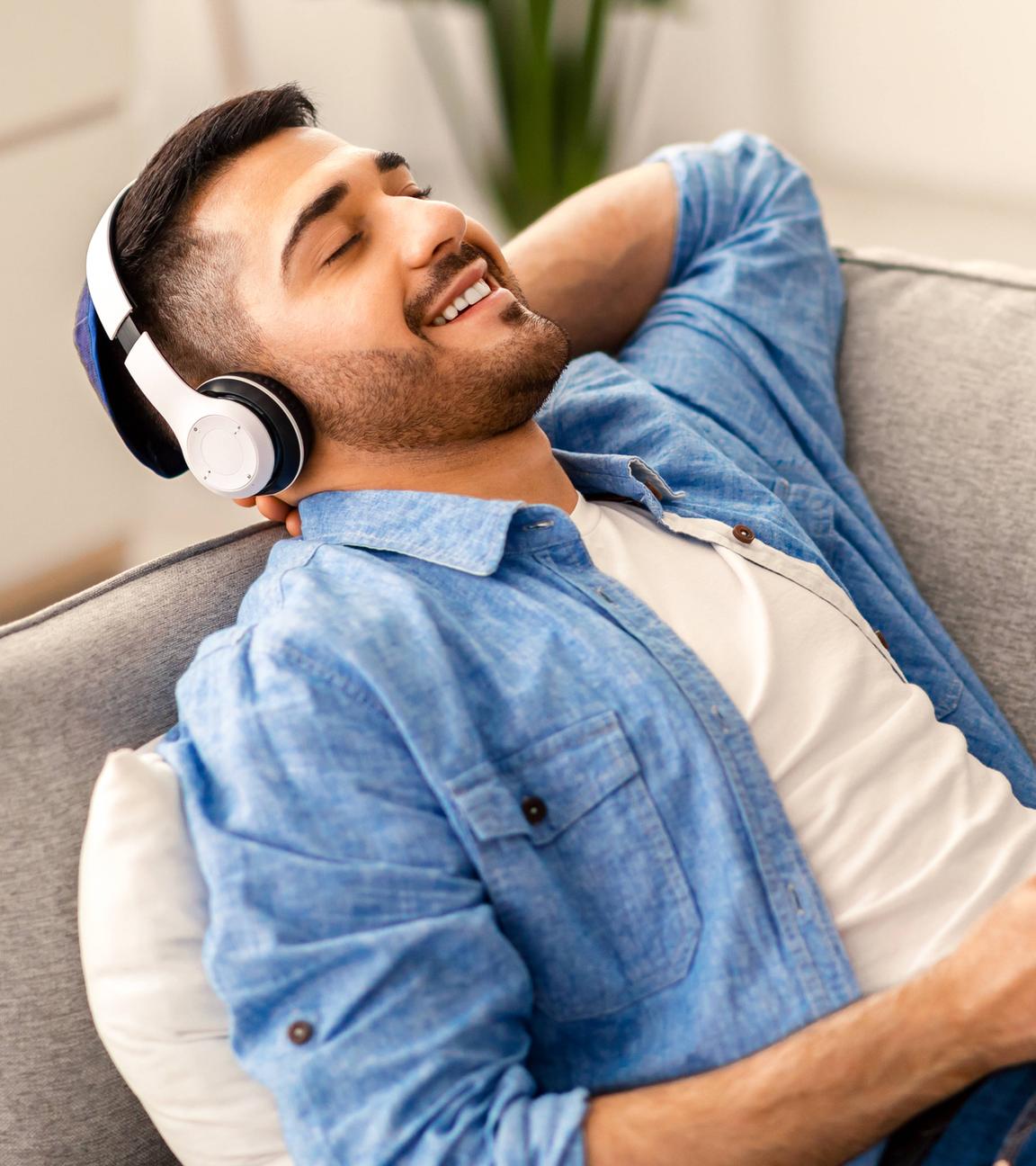 Ein Mann liegt auf einem Sofa und hört Musik über Kopfhörer und Samrtphone.