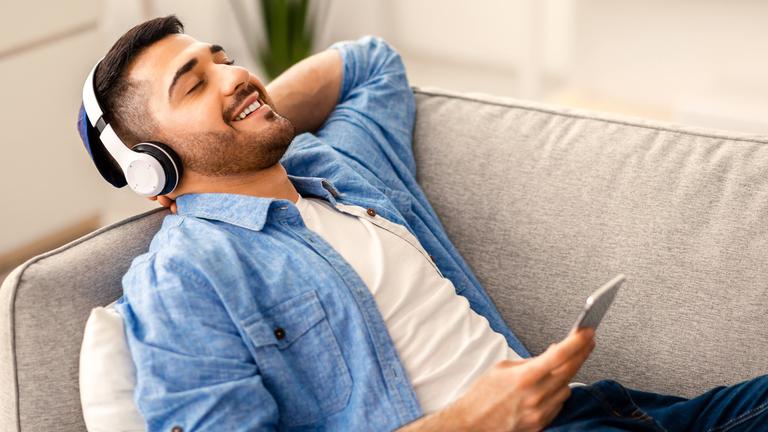 Ein Mann liegt auf einem Sofa und hört Musik über Kopfhörer und Samrtphone.