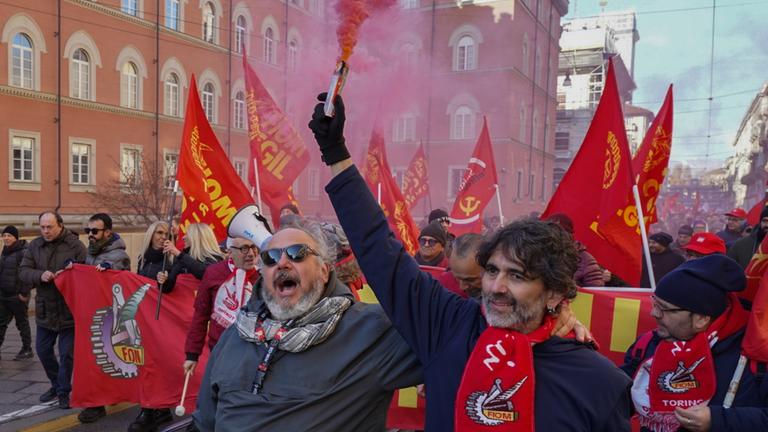 Demonstranten mit Rauchfahnen sind in Turin auf einer Straße unterwegs. In Italien hat ein großangelegter Streik gegen die Haushaltspläne der Rechtsregierung von Ministerpräsidentin Meloni begonnen.