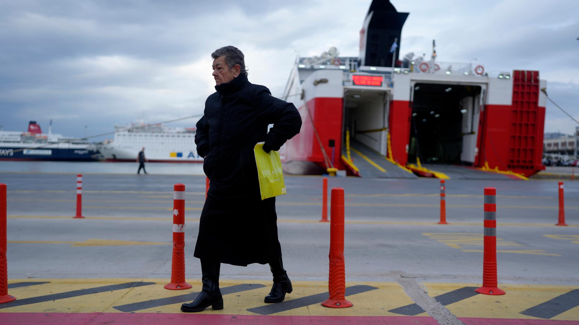 Eine Frau geht vor den Fähren spazieren, während die Fähren im Hafen von Piräus in der Nähe von Athen verankert bleiben.