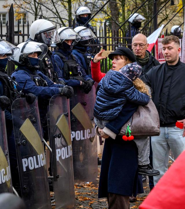 Eine Frau, die ein Kind trägt, steht vor Polizisten in Polizeiausrüstung, während sich Demonstranten vor dem Hauptsitz des polnischen Verfassungsgerichts in Warschau versammeln, nachdem die Polizei am 31. Oktober 2026 den Zugang zum Gebäude blockiert hatte.