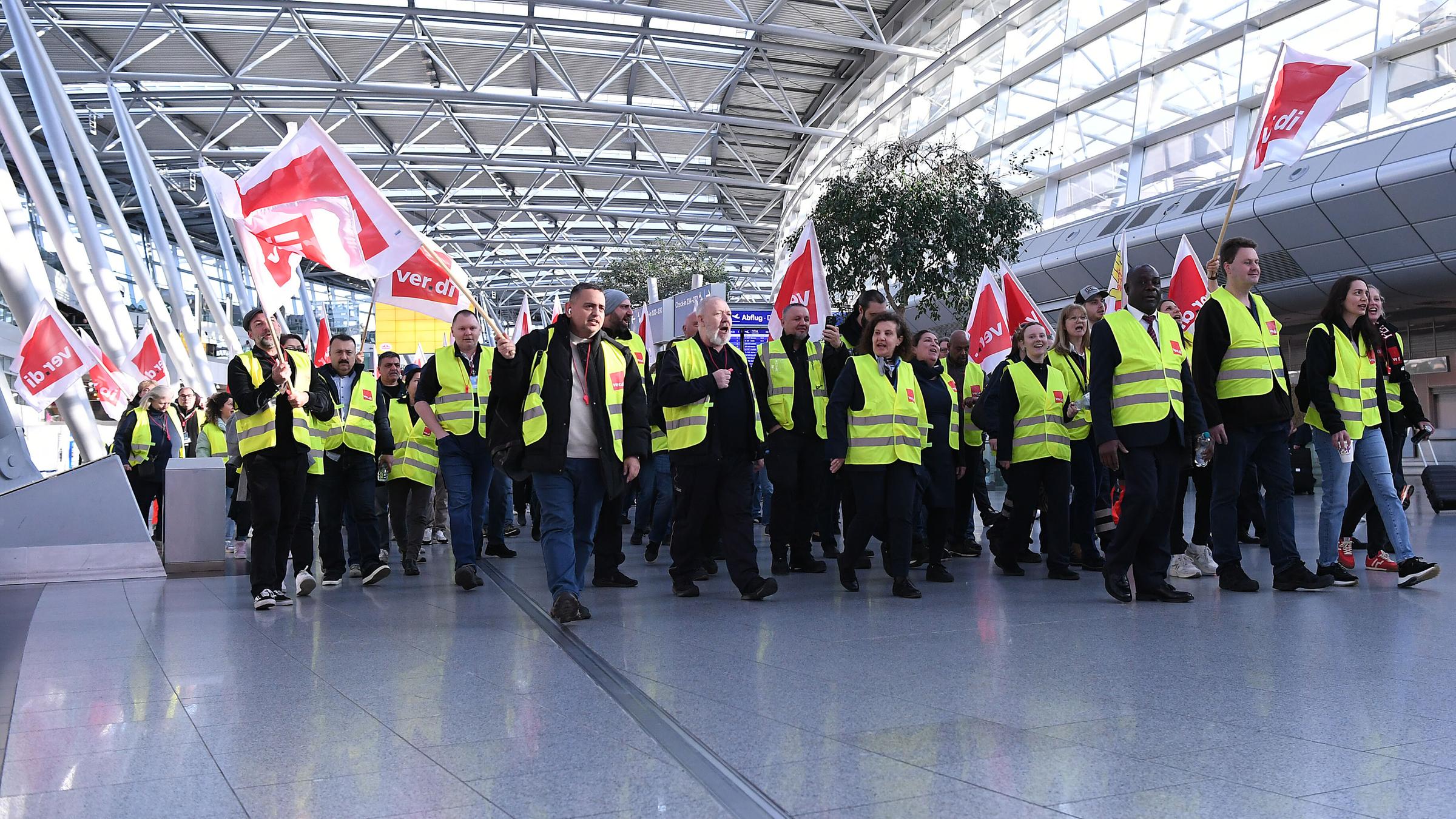 Mitglieder der Gewerkschaft Verdi laufen mit Fahnen bei einem Streik in einem Teminal des Düsseldorfer Flughafens.