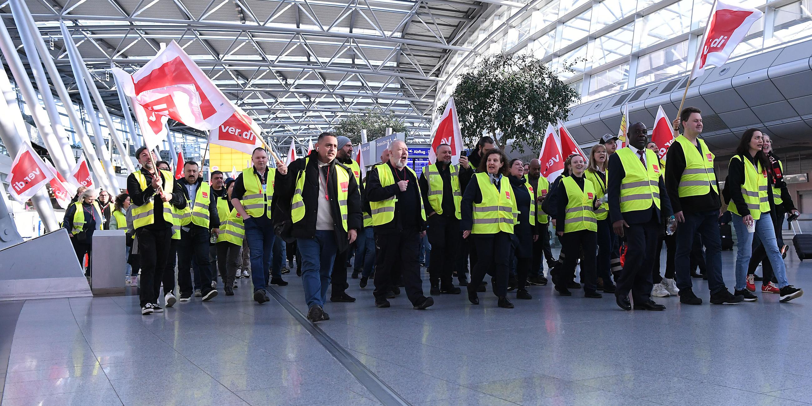 Mitglieder der Gewerkschaft Verdi laufen mit Fahnen bei einem Streik in einem Teminal des Düsseldorfer Flughafens.